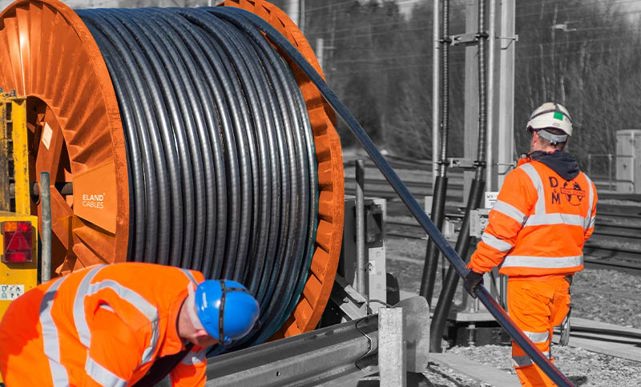 Engineers working on a railway electrification moving a large drum with railway cables